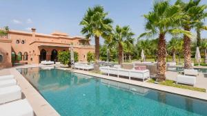 a swimming pool with white chairs and palm trees at Dreamcation Villa in Marrakesh +2 photos