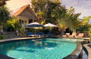 a swimming pool in front of a house with chairs and umbrellas at The Dafish Ceningan in Nusa Lembongan