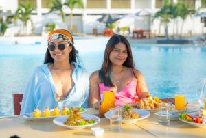 two women sitting at a table with food next to a pool at Amotape Hotel in Zorritos