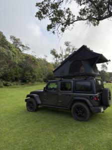 a black jeep parked in a field with its roof up at Kauai Explorer Camp Rooftop Camper fully equipped in Anahola