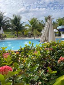 a pool with a white umbrella and some palm trees at Garden em Guarajuba in Tareco