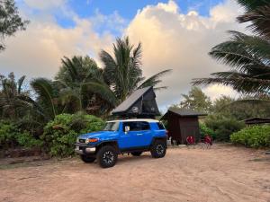 a blue truck parked on the beach with a surfboard on top at Kauai Adventure fully equipped FJ Cruiser Rooftop Camper in Anahola