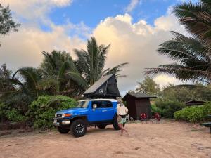 a person standing next to a blue truck on a beach at Kauai Adventure fully equipped FJ Cruiser Rooftop Camper in Anahola