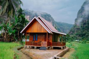 a small cabin in a field with mountains in the background at Livio Homestay in Andalas