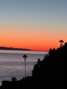 a sunset over the water with two palm trees at Paradise By The Sea in Taormina