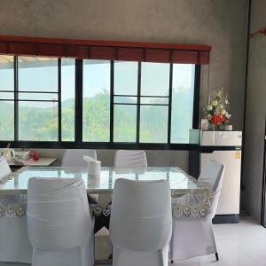 a dining room with a glass table and white chairs at Phu Man Mhok Khao Yai in Ban Nong Takhain
