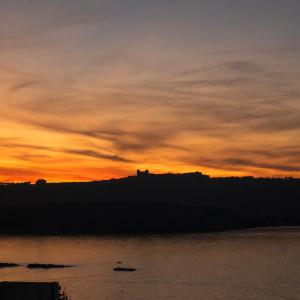 a sunset over the water with a castle in the distance at Moonlit Terrace Escape in St. Paul's Bay