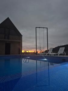 a swimming pool with two chairs and the sunset at Close to the sky in Agara +10 photos