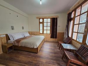 a bedroom with a bed and a chair and windows at Hotel Lady of Keylong in Kyelang +7 photos