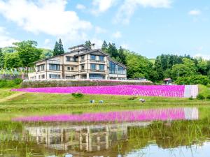 a house with pink flowers in a field next to a body of water at Eshin no Sato Yasuragisou in Joetsu