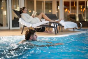 a man in a swimming pool with a woman reading a book at Hotel Trattnig in Döbriach