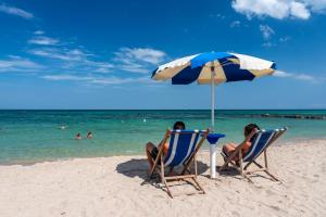 two people sitting in chairs under an umbrella on the beach at Racar Hotel in Frigole