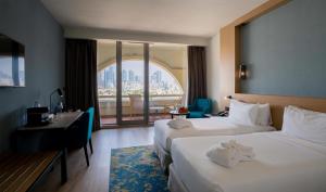 a hotel room with two beds and a desk and a window at Occidental Sharjah Grand in Sharjah