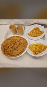 three plates of pancakes on a table with cups of coffee at MadCrew GuestHouse in Islamabad