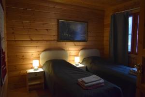 two beds in a wooden room with two lamps at Poropelto Cottage in Ruhtinaansalmi