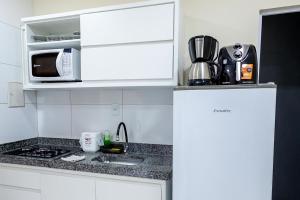 a white kitchen with a sink and a microwave at Studio Completo c Wifi perto do Centro de Itabuna in Itabuna +4 photos