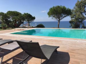 a swimming pool with chairs and the ocean in the background at Villa Edo Cefalù in Cefalù