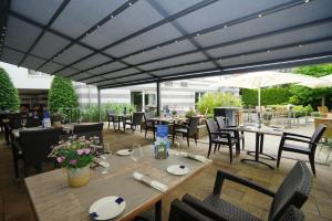 eine Terrasse mit Tischen, Stühlen und einem Sonnenschirm in der Unterkunft Ringhotel Appelbaum Gütersloh in Gütersloh