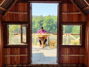 a man sitting at a table in a house through a window at Bonomali Mangrove Resort in Dhāngmāri Forest Office