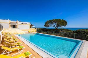 a swimming pool with chairs and an umbrella and the ocean at Casa Benagil Mar by Algarve Holidays in Lagoa