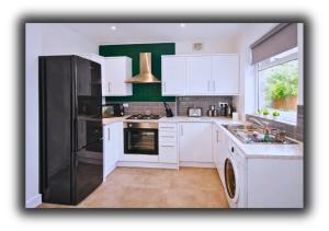 a kitchen with white cabinets and a black refrigerator at Pitchside House Walk to Anfield sleeps 7 in Liverpool