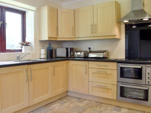 a kitchen with wooden cabinets and black appliances at The Oaks - Uk11270 in Lanreath