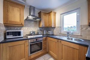 a kitchen with wooden cabinets and a sink and a microwave at Charming & Cosy Drymen Flat in Drymen