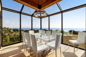 a dining room with white chairs and a table and glass windows at Breakers Retreat in Sea Ranch