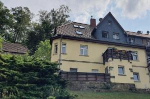 a large yellow house with a black roof at Ferienwohnung Menz Liliensteinblick in Pfaffendorf