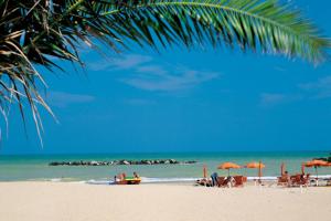 a beach with people sitting under umbrellas and the ocean at BLU CORALLO in Porto San Giorgio