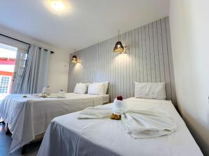 two beds in a hotel room with white sheets at Pousada Arte do Velejo by Solarium in São Miguel do Gostoso