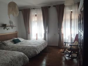 a bedroom with two beds and a chair and windows at El rinconcito in Fuenteheridos