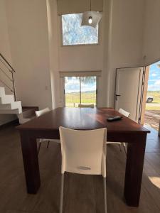 a dining room table with white chairs and a window at Complejo del Jagüel Cabaña Virginia in Santa Teresita