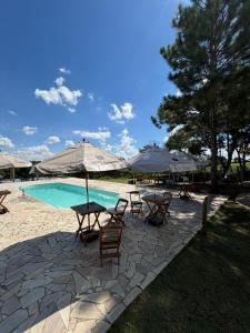 ein Schwimmbecken mit Stühlen und Sonnenschirmen sowie einem Tisch und Stühlen in der Unterkunft Chalé do Rista in Suzano