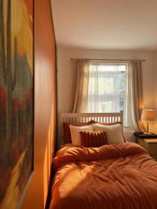 a bedroom with a bed with an orange comforter and a window at Hotel Style Room within Reading in Reading