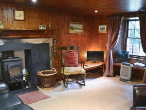 a living room with a fireplace and a chair and a desk at Gardener's Bothy in Balnaboth