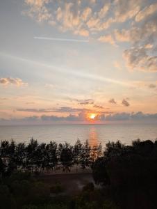 a sunset over the ocean with trees in the foreground at Seaview Turtle Cove in Kampong Bugis