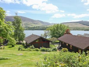 two cottages with a lake and mountains in the background at Loch Earn View Lodge in Lochearnhead