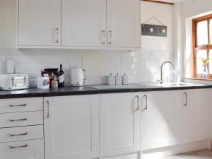 a white kitchen with white cabinets and a sink at Woodpecker Rest in Cilgerran +13 photos