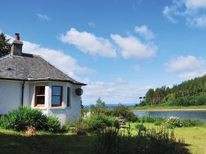 a small white house in the grass next to a river at Shore Cottage - S4600 in Tarbert