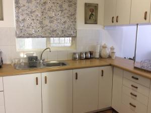 a kitchen with white cabinets and a sink and a window at On Broadwalk Cottage in Cape Town