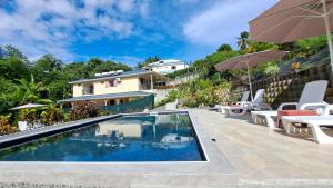 a swimming pool with chairs and umbrellas next to a house at Résidence Paradis in Petit-Bourg