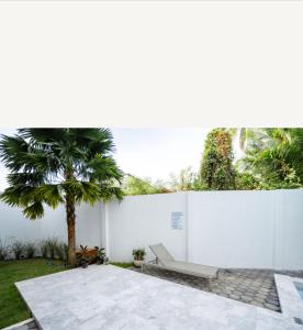 a white wall with a bench and a palm tree at La Cha Cha Residence in Ban Thalat Choeng Thale