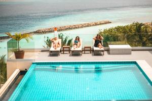 three women sitting in chairs next to a swimming pool at Season Paradise in Thulusdhoo