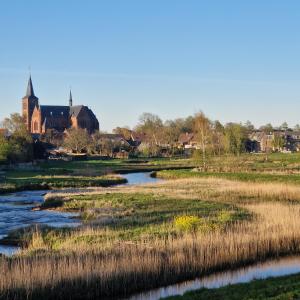 a river in a field with a church in the background at B&B Chez Paz in Neer