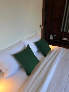 a white bed with two green pillows on it at ค้างคาวกินกล้วยโฮมสเตย์ in Ban Mung
