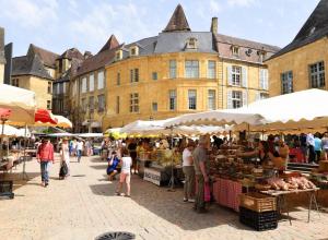 a group of people walking around a market in front of a building at La Salamandre - Un écrin médiéval pour vos souvenirs - Imaginez-vous, réveillé par le murmure de Sarlat, dans un appartement spacieux et chaleureux, au cœur de la Cité classée - 2 chambres - Une magie à vivre sans modération - Réservez dès maintenant ! in Sarlat-la-Canéda