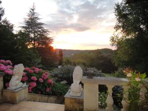 een tuin met beelden en bloemen met de zonsondergang op de achtergrond bij Le Tambourinet in Belvès