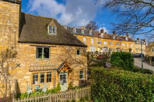 an old stone house with a fence in front of it at 4 Crown Cottages in Moreton in Marsh