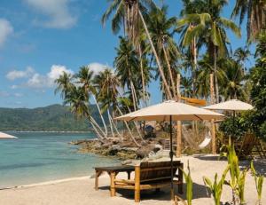ein Strand mit einer Bank und Sonnenschirmen und dem Meer in der Unterkunft Camp Laya Daracoton Island in El Nido